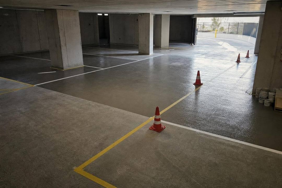Tiefgarage mit weißen und gelben Stellplatzmarkierungen auf Betonboden, dazwischen Verkehrsleitkegel.