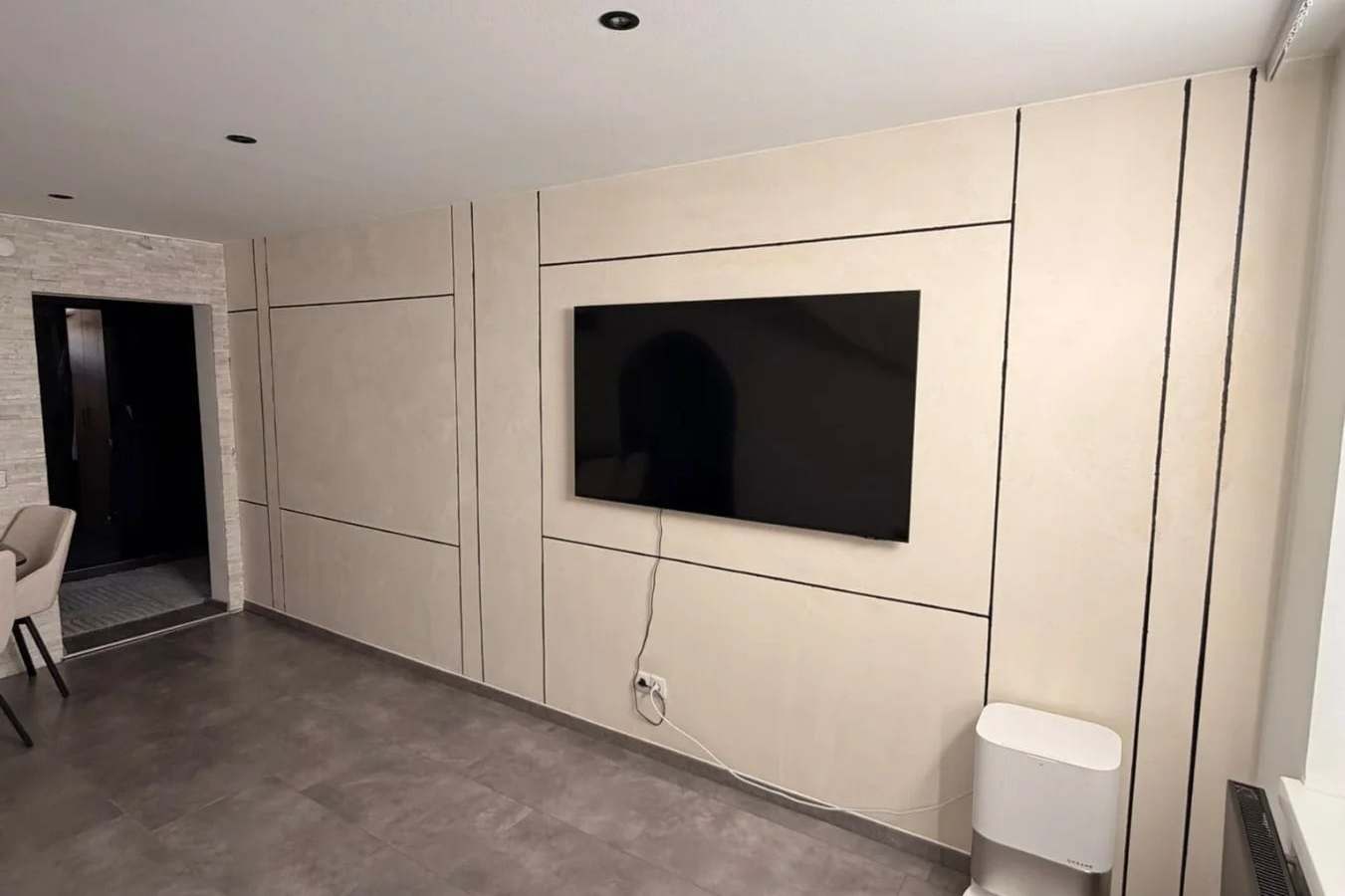 Wohnwand in fugenlosem Mikrozement mit warmer Wolkenstruktur, davor ein wandhängender Fernseher.