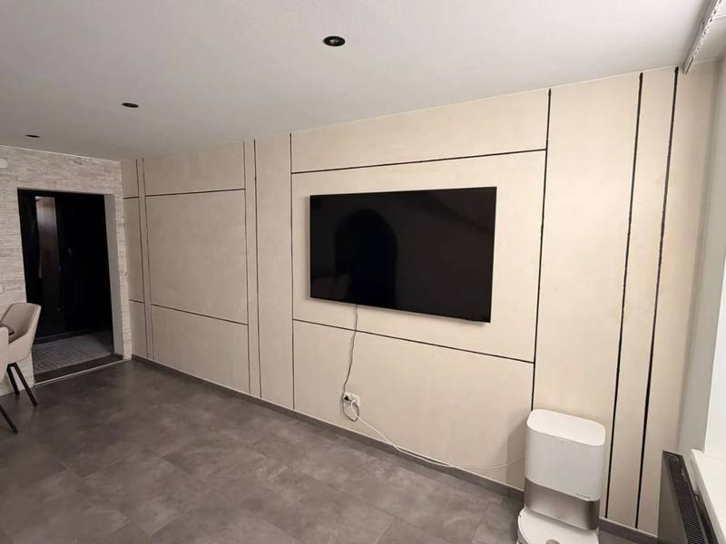 Wohnwand in fugenlosem Mikrozement mit warmer Wolkenstruktur, davor ein wandhängender Fernseher.