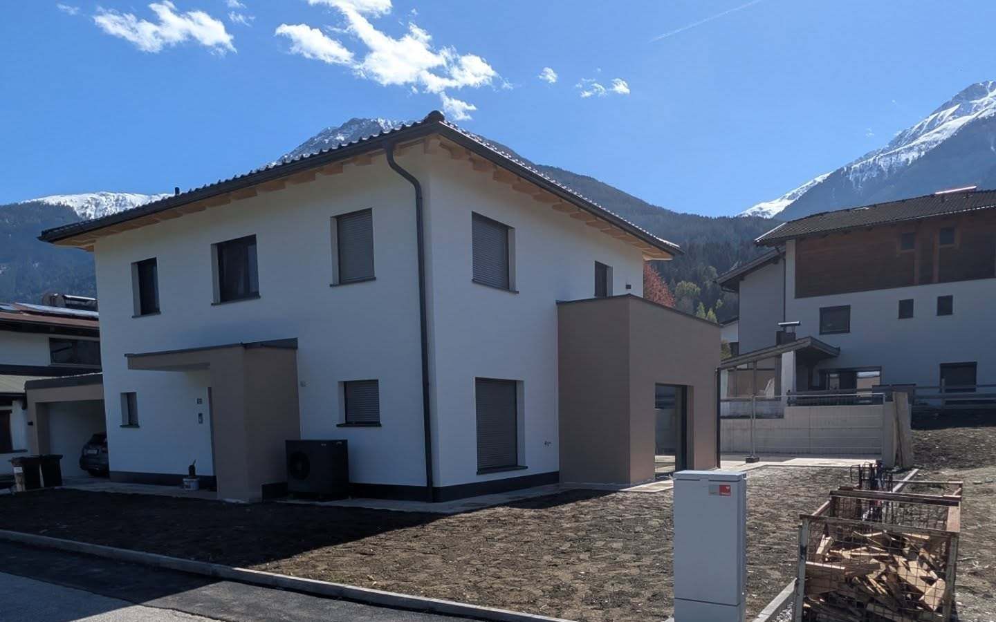 Frisch gestrichene weiße Fassade eines Neubaus in Tirol mit abgesetztem Farbton am Anbau, Berge im Hintergrund.