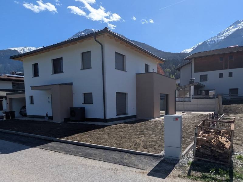 Frisch gestrichene weiße Fassade eines Neubaus in Tirol mit abgesetztem Farbton am Anbau, Berge im Hintergrund.