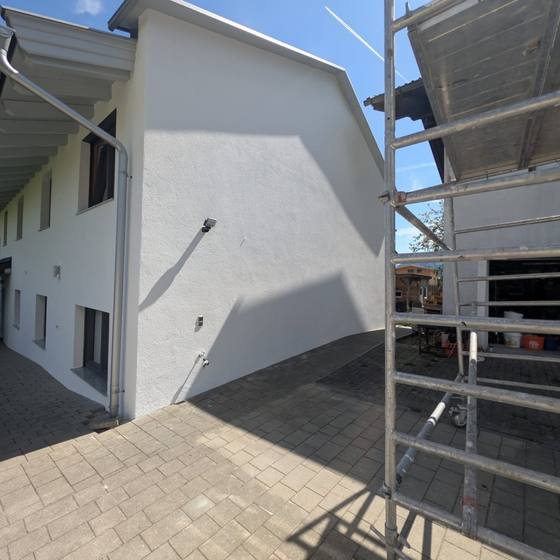 Weiße Fassade mit Rollgerüst als Zugang zu Dachrand und Holzuntersicht während der Anstricharbeiten.