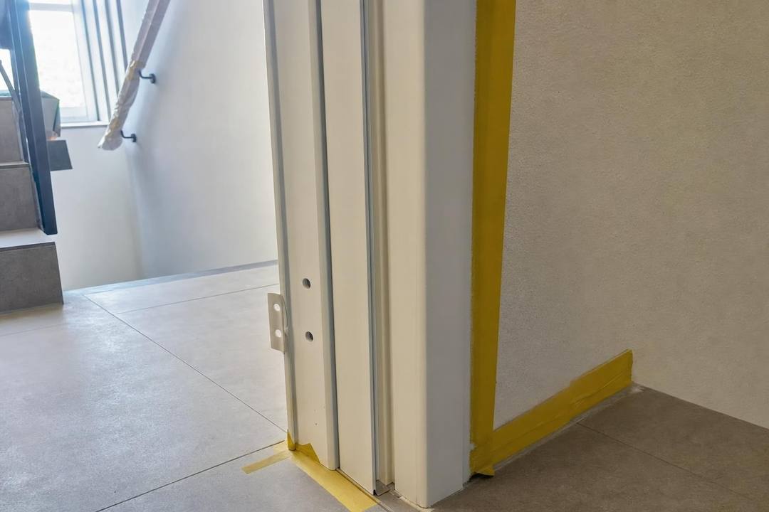 Weiß lackierte Türzarge im Detail, an der Wand und am Boden mit gelbem Kreppband abgeklebt.