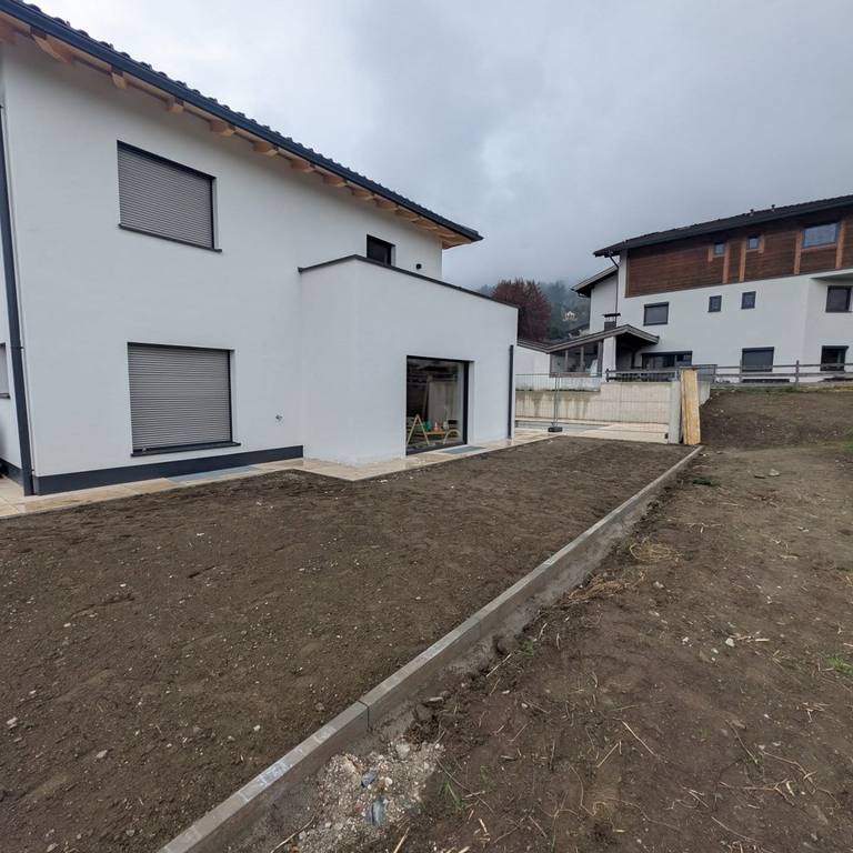 Neubau in Tirol vor dem Fassadenanstrich, bei bedecktem Himmel; das Grundstück ist noch Baustelle.